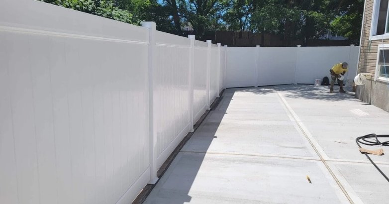 A worker installs a white fence in a backyard, adhering to fencing regulations in New York City and New Jersey.