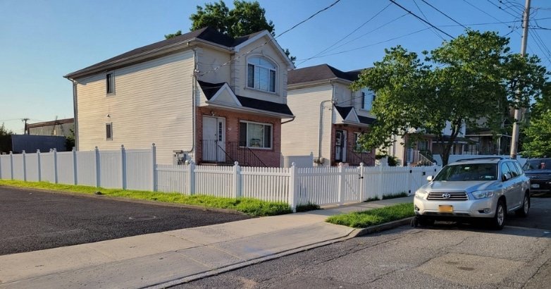 A white fence surrounds a house with a car parked in front, illustrating residential zoning in New York City and New Jersey.