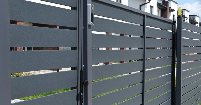A black slatted fence with a gate, showcasing modern fencing trends in urban environments.