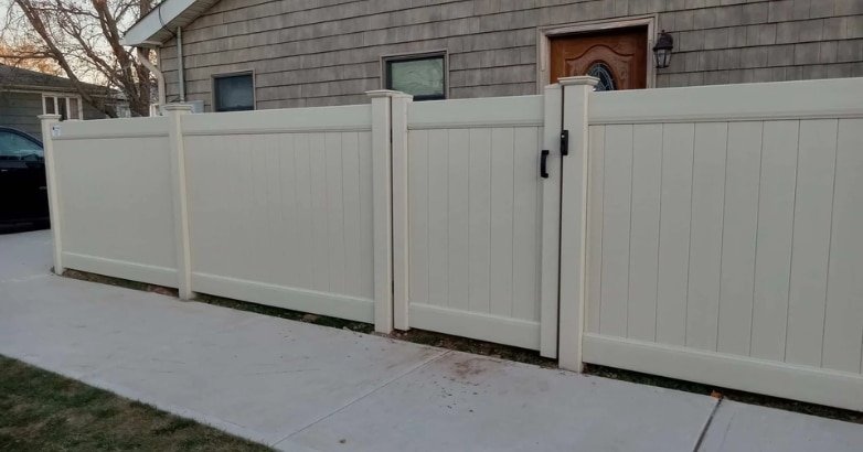 A white fence made of vinyl is positioned in front of a house, highlighting urban custom fencing solutions.