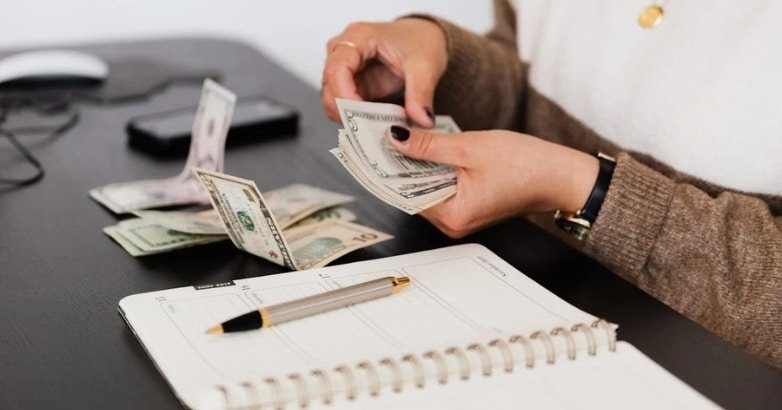 A woman counts cash on a desk, reflecting on budget considerations for choosing a driveway gate for her home.