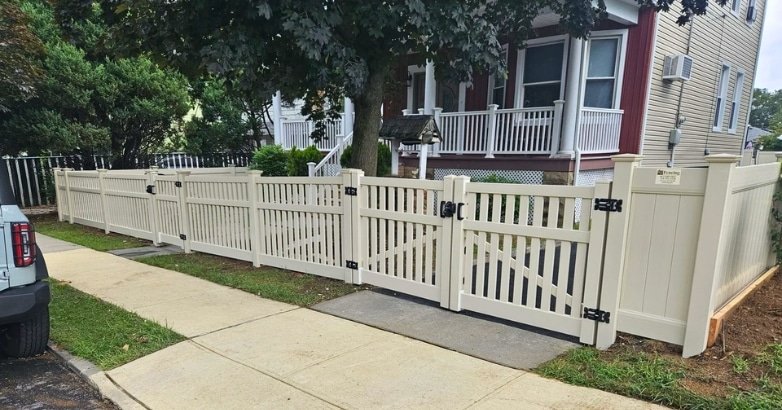 A white fence with a gate and a car in front, highlighting considerations for choosing the right driveway gate materials.