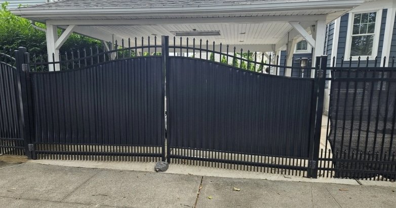 A black wrought iron gate stands in front of a house, symbolizing security and elegance for driveway gate choices.