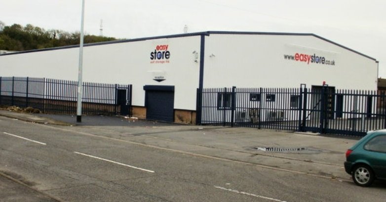 A white building with a fence and parked cars, highlighting modern business solutions with automated gates for cost savings.