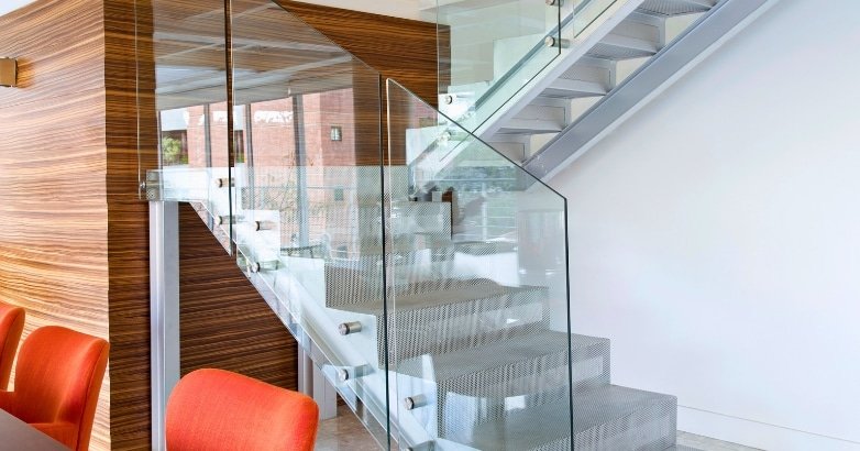 Interior view of a glass stairway with orange chairs and a table, highlighting contemporary railings in New York.
