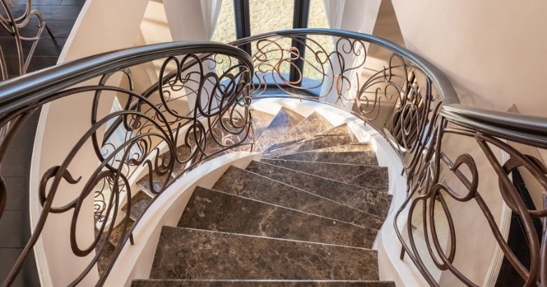 A beautifully designed spiral staircase with marble and wrought iron handrails, showcasing intricate scrollwork in New York.