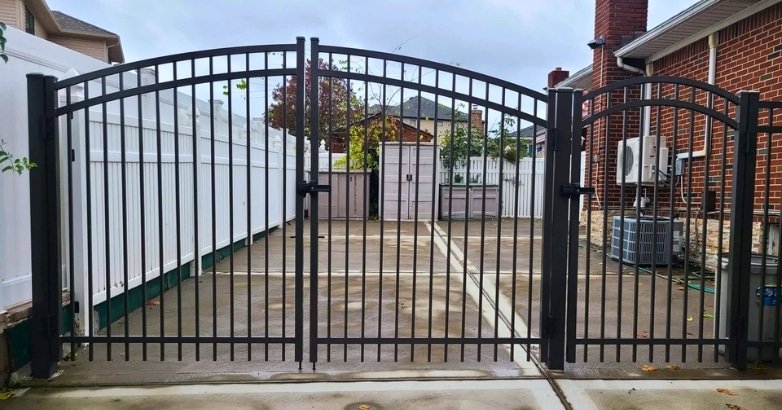 A black wrought iron gate in a backyard, showcasing Five Boroughs Fencing Solutions for commercial aluminum fencing.