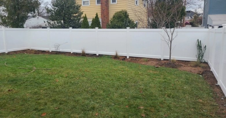 A well-maintained white fence encloses a lush lawn in a backyard, providing privacy and a polished look.