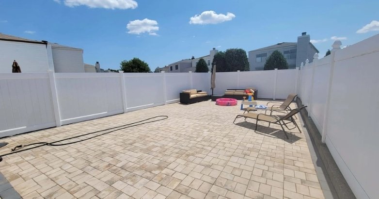 A backyard featuring a brick patio surrounded by a white fence, highlighting a durable outdoor space for year-round enjoyment.