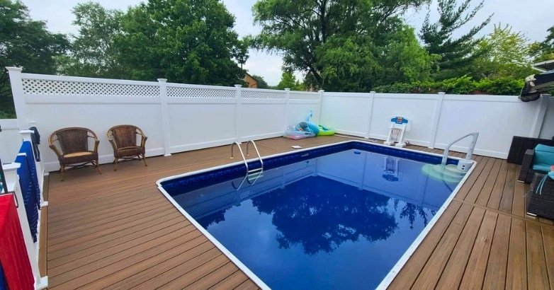 A serene pool surrounded by a wooden deck and a white fence, highlighting the importance of quality fencing for maintenance.