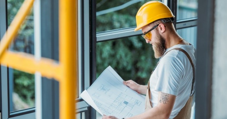 A man in a hard hat and yellow glasses examines a blueprint, emphasizing the importance of professional railing installation.