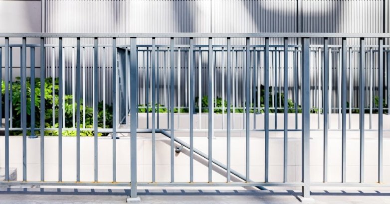 A metal fence with a gate and wall, illustrating the concept of exterior railings in an architectural context.