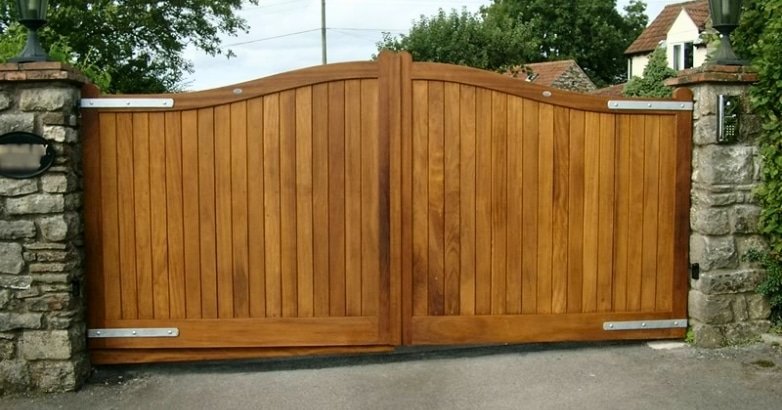 A wooden swing gate set against a sturdy stone wall, enhancing the curb appeal of a residential property.
