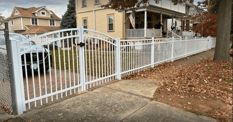 A white fence with a decorative gate stands in front of a house, enhancing its curb appeal with a stylish design.