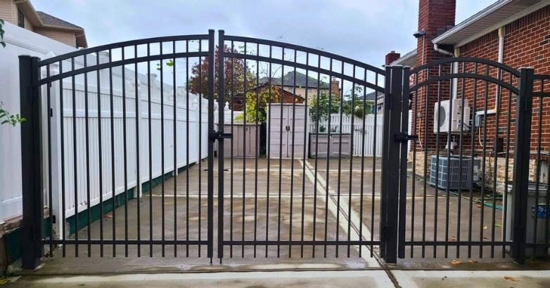 Comparing Commercial Fencing Materials Aluminum A black aluminum gate and fence stands in a backyard, showcasing a decorative design and providing access to the outdoor space.