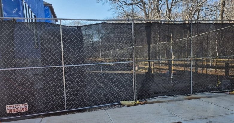 Comparing Commercial Fencing Materials Chain Link A chain link fence is being installed around a house, illustrating the process of commercial fencing material application.