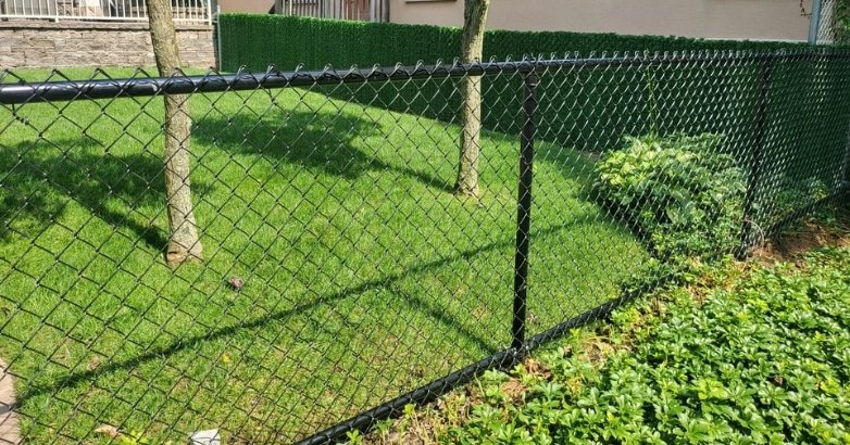 Checklist for Planning a Fencing Project Chain link Fence A black chain link fence in a yard, depicting an example for a checklist on planning a fencing project.