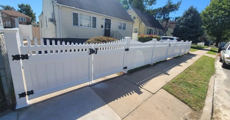 Sloped Driveway Gate Installation Ignore Local Codes and Safety Standards A white picket fence featuring a black gate, underscoring the need to follow local codes and safety standards during installation.