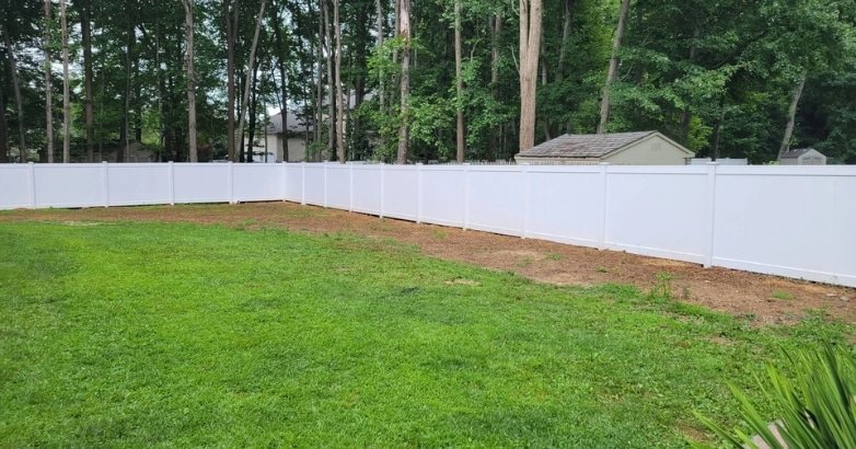 A white fence in a grassy backyard with trees, showcasing a potential budget-friendly fencing project.