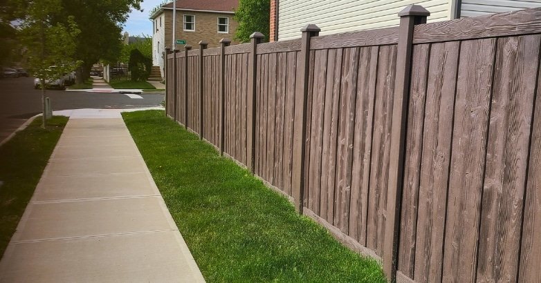 A brown wooden fence stands beside a concrete sidewalk, illustrating the importance of upgrading old fencing.