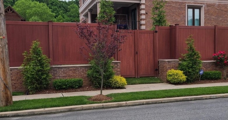 Seasonal Fencing Maintenance in New York JR Fencing A composite fence with a bright red gate and green bushes, illustrating seasonal fencing maintenance by JR Fencing in New York.